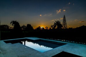 A swimming pool with a clear reflection, surrounded by a tiled deck and palm trees, under a sunset sky. - Hotel Palma Verde (Armenia)