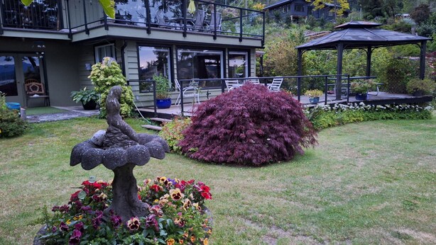Una casa moderna con un patio, un mirador y un jardín con una escultura de pájaro y flores coloridas.