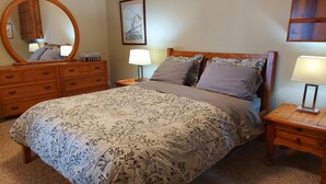 Un dormitorio ordenado con una cama grande, un aparador de madera, una mesita de noche con lámpara y un espejo montado en la pared.
