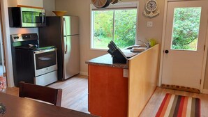 Cocina compacta equipada con refrigerador, microondas y horno, y una ventana con vista a follaje.