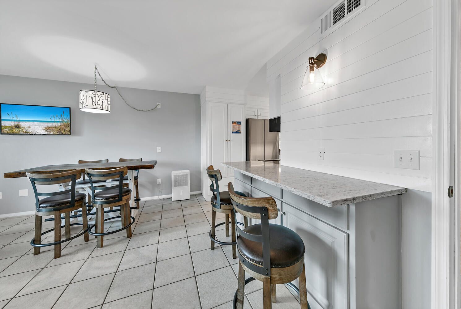 Una cocina moderna con armarios blancos, encimera de mármol y comedor con sillas y mesa de madera.