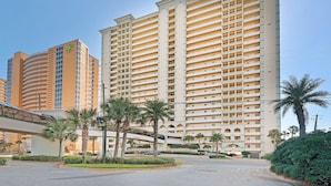 A high-rise hotel with multiple balconies, a covered walkway, and palm trees.