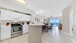 A modern kitchen with white cabinets, a built-in oven, and a dining area with a view of the ocean.