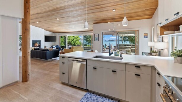 Une cuisine moderne dotée d’un îlot central, d’un plafond en bois et de grandes fenêtres offrant une vue sur l’extérieur.