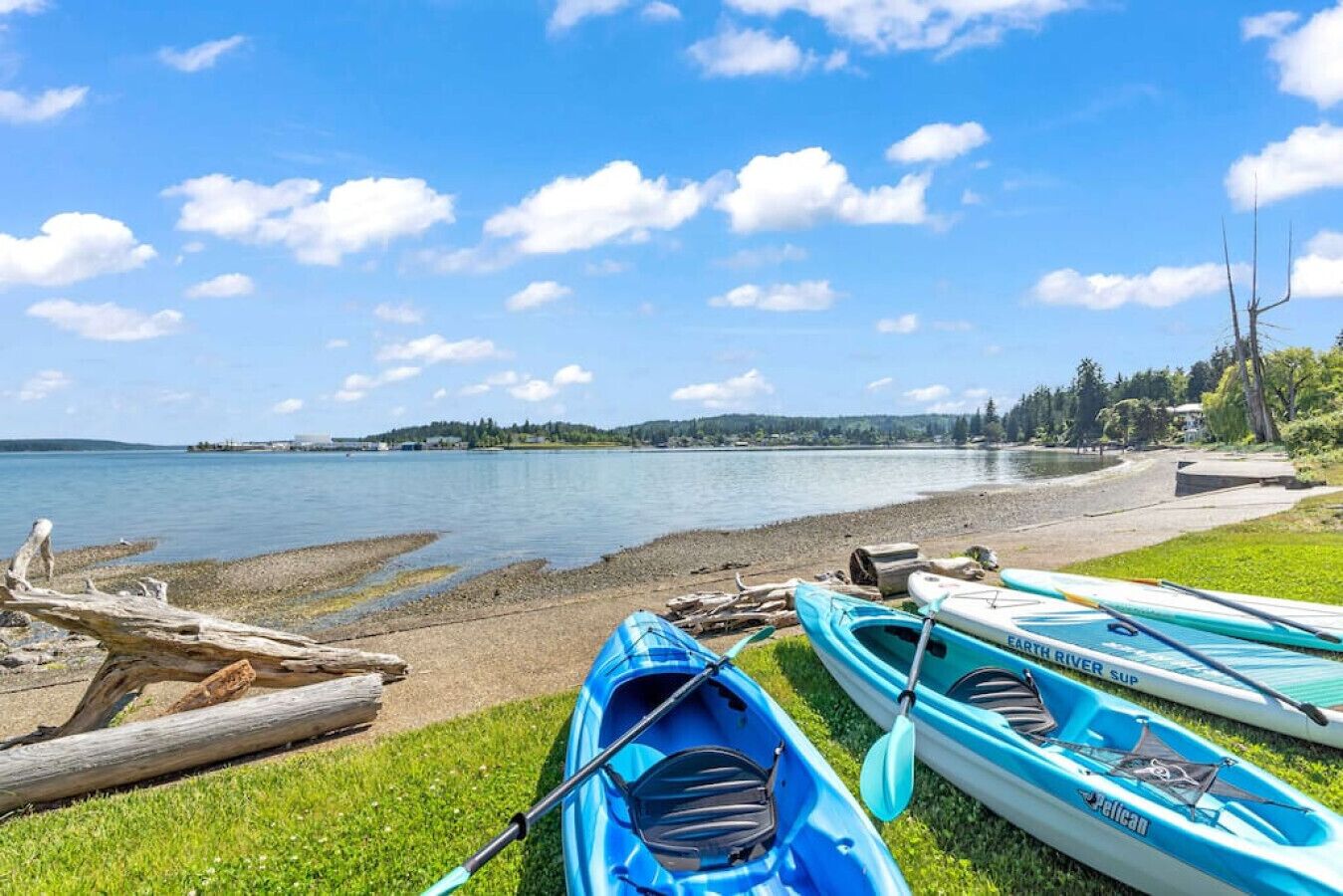 A lakeside view with kayaks and a paddleboard on the shore, a grassy area, and a clear sky.