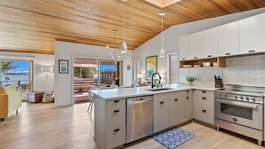 Une cuisine moderne dotée d’un grand îlot central, d’appareils électroménagers en acier inoxydable et offrant une vue sur l’extérieur.