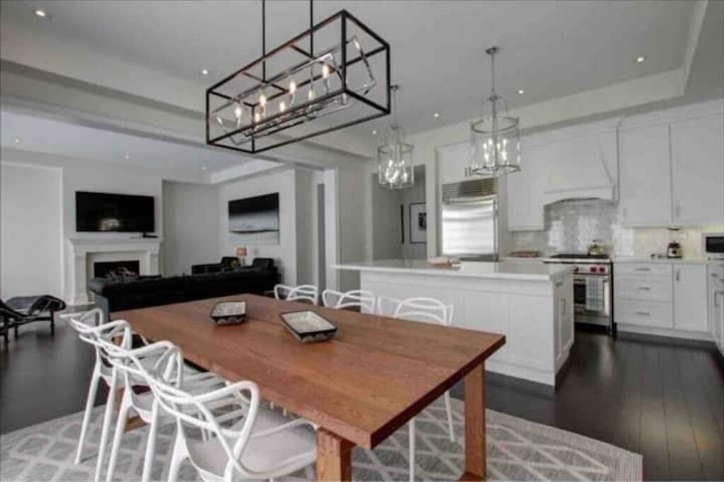 Une cuisine moderne avec des meubles blancs, une table à manger en bois et des luminaires suspendus.
