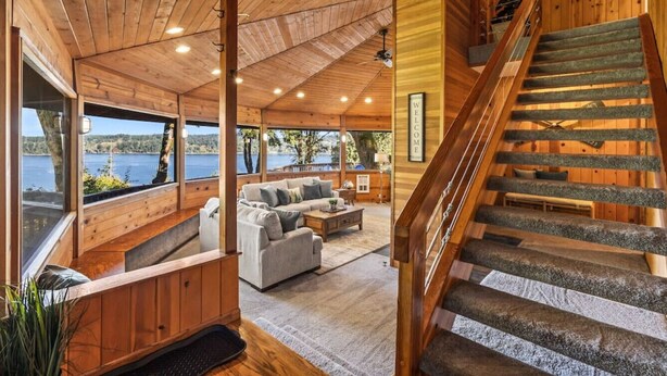A wooden cabin interior with a living area, a staircase, and a view of the lake. - Eagle`s Lookout Lodge w/ Hot Tub (Gig Harbor)