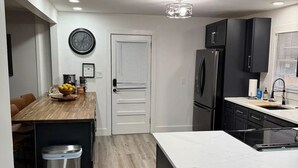 Una cocina moderna con una isla central, armarios negros y un cubo de basura de acero inoxidable.