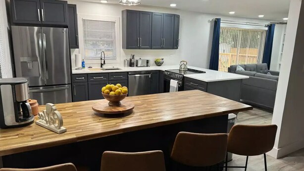 Una cocina moderna con una isla central, electrodomésticos de acero inoxidable y una zona de comedor con cuatro sillas.