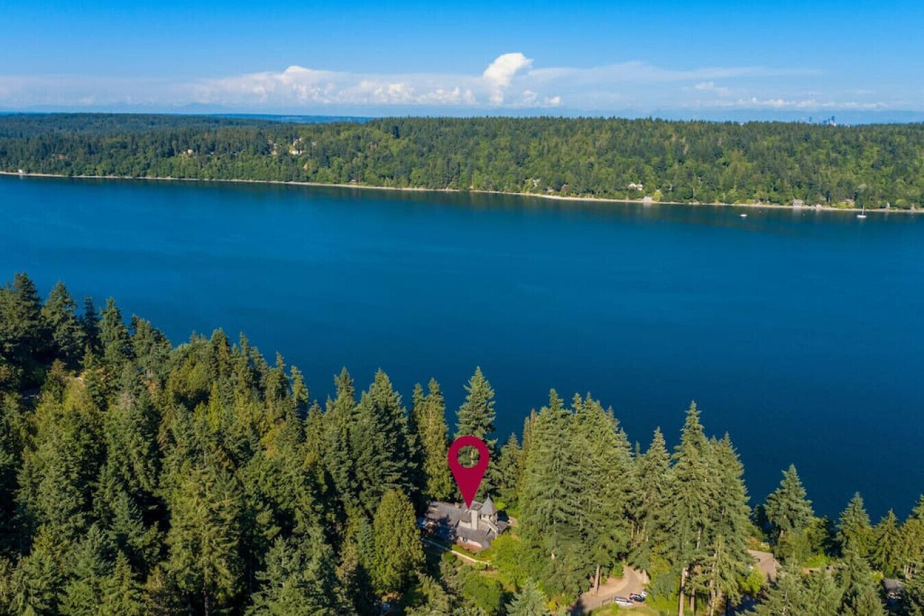 A lake surrounded by dense forest, a red marker indicating a location, and a small building with a driveway.