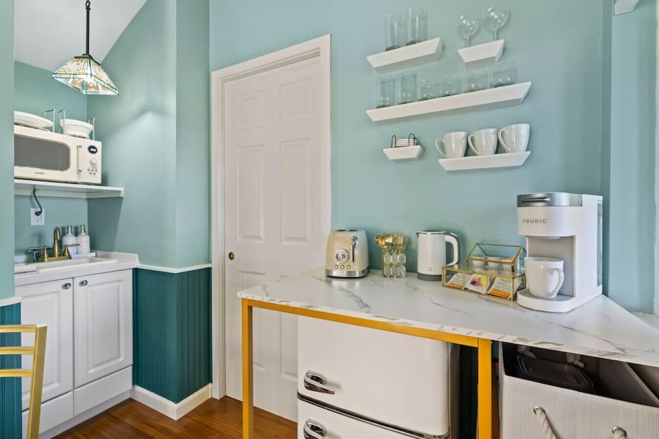 A kitchen with teal walls, white cabinets, a marble countertop, and various appliances including a microwave, toaster, kettle, and coffee maker.