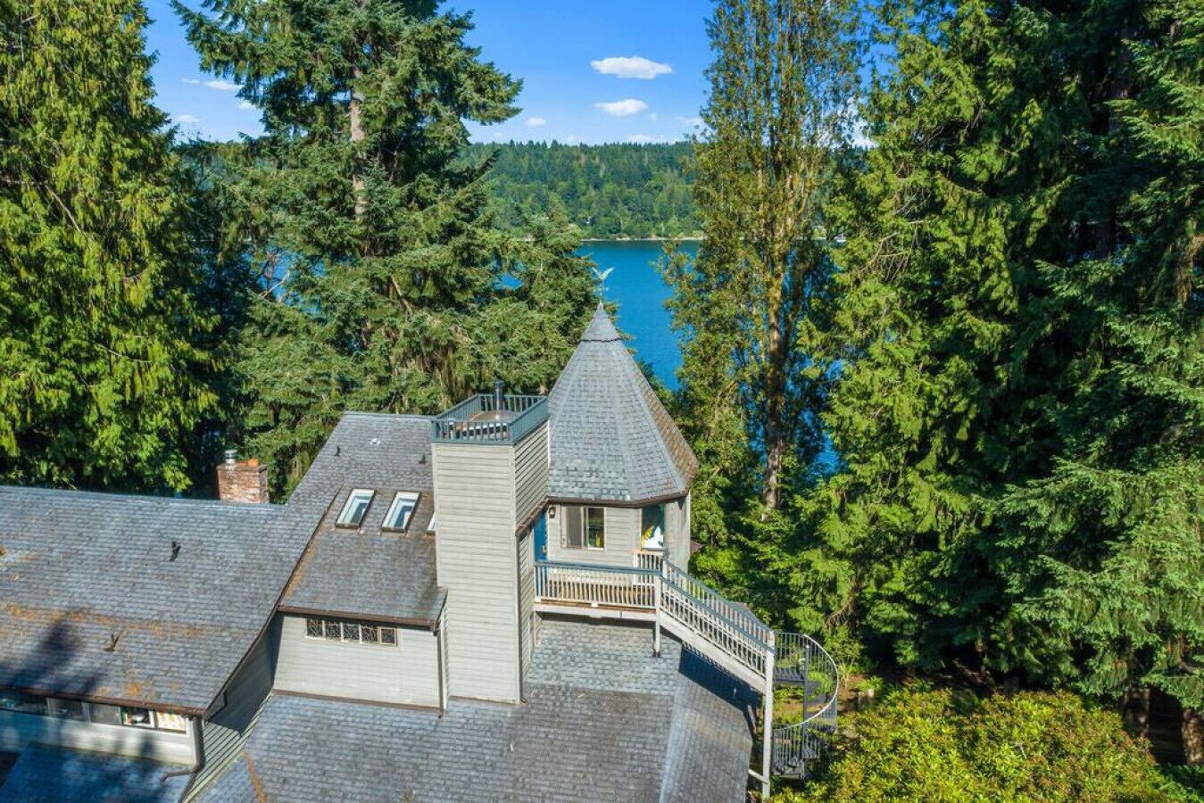 A house with a steeply pitched roof, a balcony, and a view of a lake surrounded by dense forest.