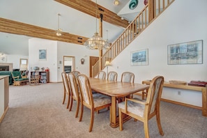 A spacious dining area with a wooden table and chairs, a staircase, and a view of the living room.