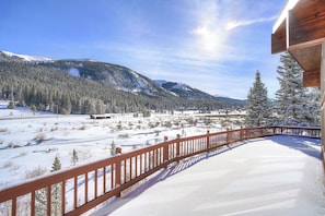 A snow-covered landscape with a wooden deck and a mountain backdrop.