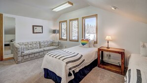 A bedroom with a bed, a sofa, a bedside table, and a window with a view of trees. - Evans Mountain Lodge (Breckenridge)
