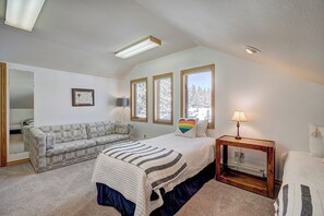 A bedroom with a bed, a sofa, a bedside table, and a window with a view of trees. - Evans Mountain Lodge (Breckenridge)