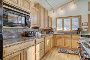 Une cuisine avec des meubles en bois, un four à micro-ondes, un grille-pain et une grande fenêtre donnant sur un paysage enneigé.