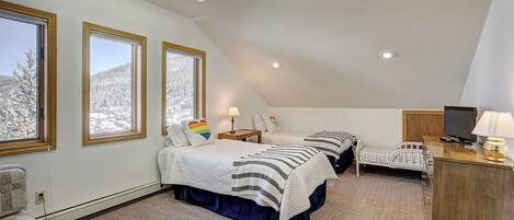 A cozy attic bedroom with two beds, a desk, and a TV.