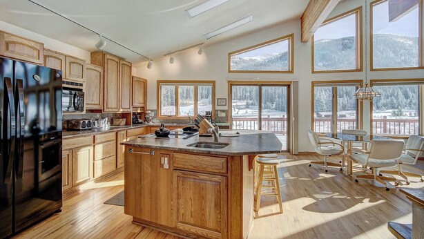 A spacious kitchen with wooden cabinets, a large island, and a dining area with a view of snowy mountains. - Evans Mountain Lodge (Breckenridge)