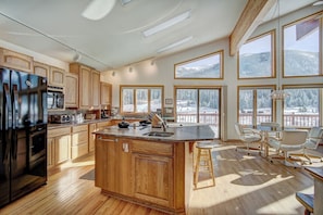 A spacious kitchen with wooden cabinets, a large island, and a dining area with a view of snowy mountains.