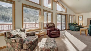 A spacious living room with large windows, a fireplace, and a view of a snowy landscape. - Evans Mountain Lodge (Breckenridge)