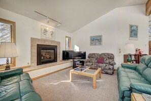 Una sala de estar con chimenea, televisor y dos sofás verdes.