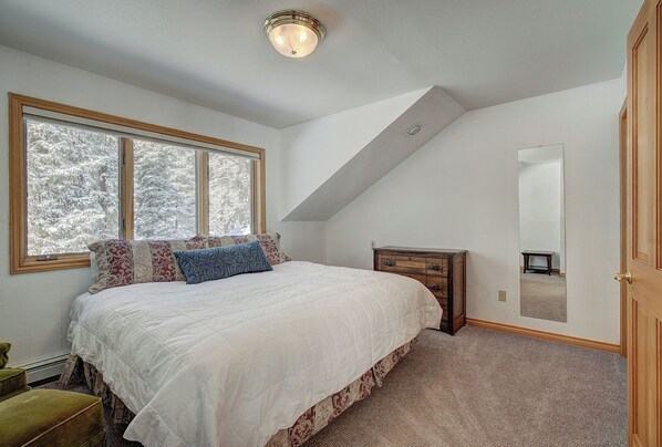 Une chambre à coucher avec un grand lit, une commode, un miroir et une fenêtre donnant sur des arbres couverts de neige.
