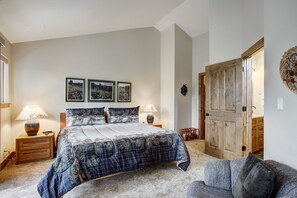 A bedroom with a bed, two bedside tables, a nightstand, a door, and a wall-mounted light fixture. - Village Point 308 (Breckenridge)