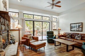 A spacious living room with a fireplace, large windows, a ceiling fan, and a wooden coffee table. - Village Point 308 (Breckenridge)