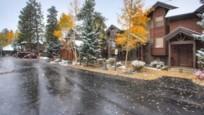 Une rue résidentielle bordée de maisons, avec une chaussée mouillée et des arbres aux feuilles d’automne.
