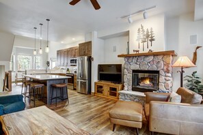 A spacious kitchen with a central island, wooden cabinets, and a stone fireplace. - Village Point 308 (Breckenridge)