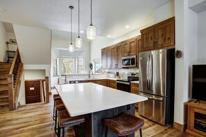 A modern kitchen with wooden cabinets, stainless steel appliances, and a large island with bar stools. - Village Point 308 (Breckenridge)