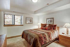 Une chambre à coucher avec un lit, une table de chevet, une lampe, une fenêtre et deux tableaux encadrés accrochés au mur.
