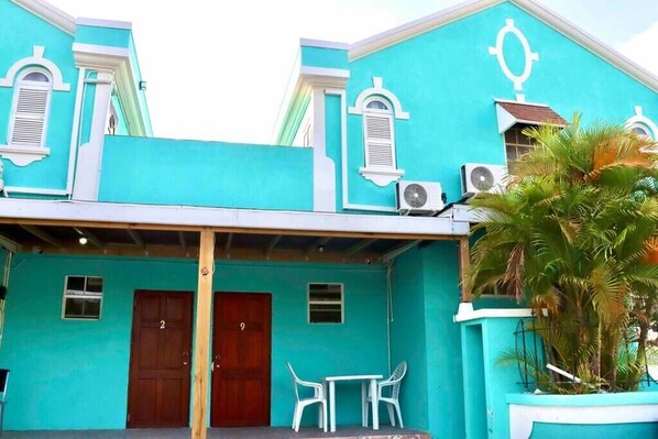 Un edificio turquesa con dos puertas, numeradas 2 y 9, y una pequeña mesa con sillas afuera.