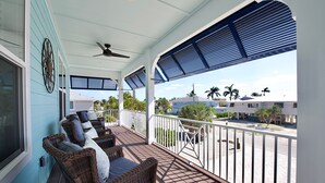 A covered balcony with wicker furniture, a ceiling fan, and a view of palm trees and buildings. - Crain's Perch will Wow you! (Fort Myers Beach)