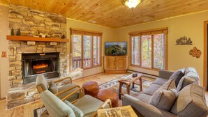 Una sala de estar acogedora con chimenea de piedra, techo de madera y ventanas amplias.