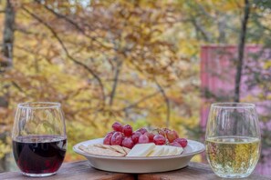 Uma mesa com um prato de queijo, uvas e biscoitos, e dois copos de vinho.