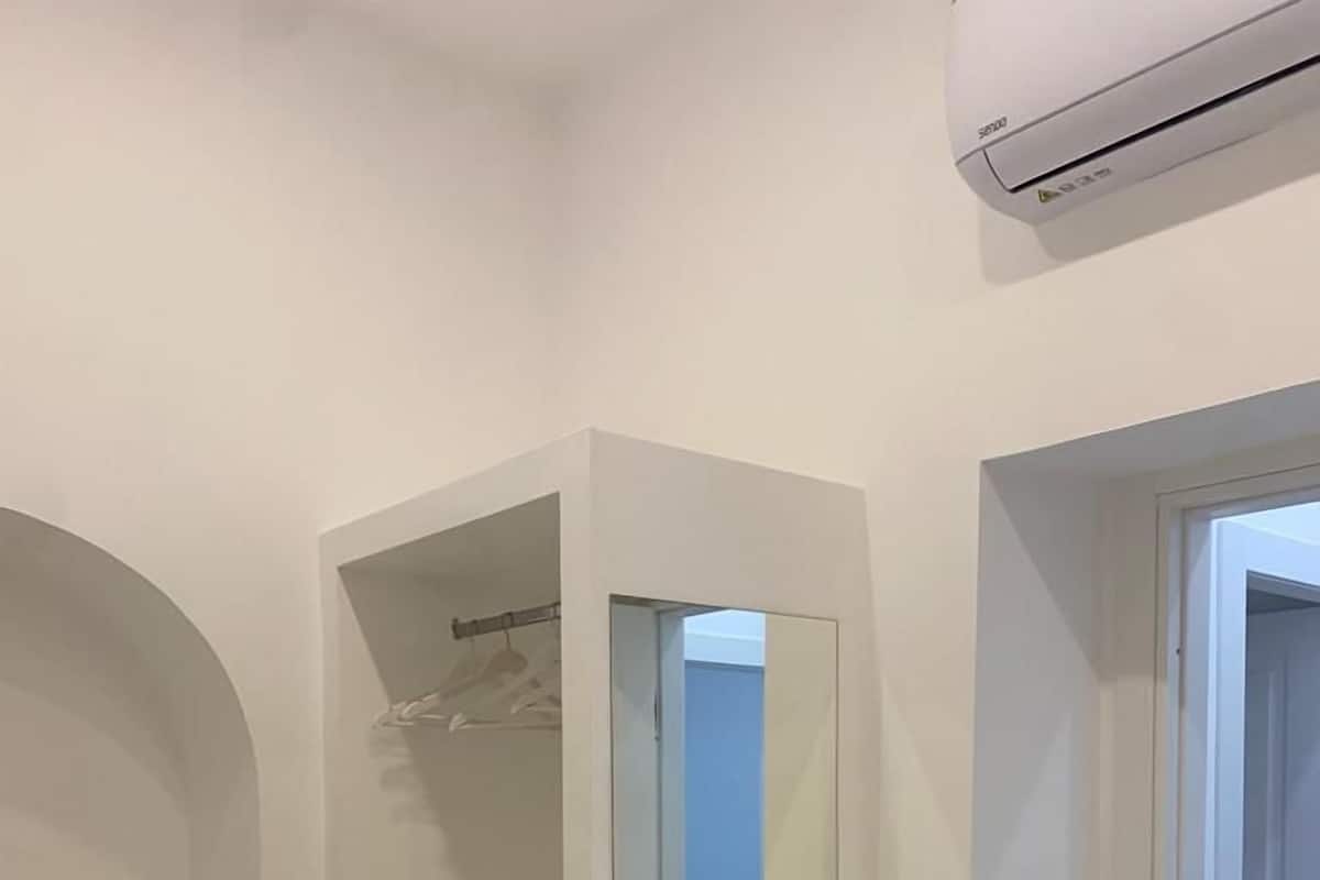Ein schmaler Flur mit einem weißen Kleiderschrank, einem Spiegel und einer Klimaanlage.