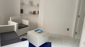 Una habitación con muebles de mimbre blancos, un estante pequeño con adornos y un piso de baldosas azules.