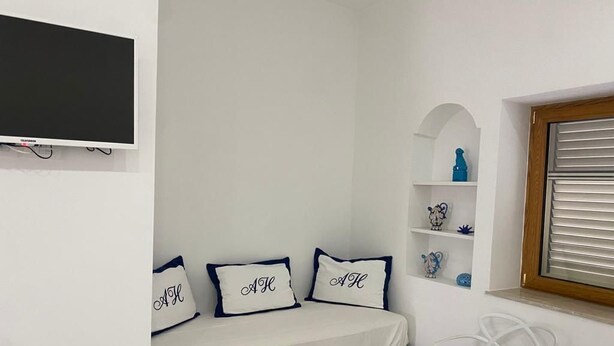 Un dormitorio con cama, televisor, repisas con adornos y una ventana con persianas.