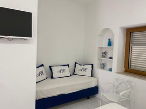 A bedroom with a bed, a TV, a shelf with decorative items, and a window with blinds. -  Abagnale Home Sorrento (Sorrento)