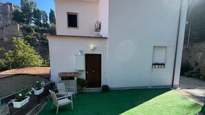 Una casa moderna con fachada blanca, césped artificial verde y un pequeño patio con puerta y ventana.