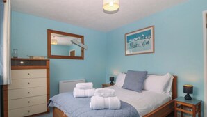 Un dormitorio con cama, cómoda, mesita de noche, lámpara, espejo y un cuadro en la pared.