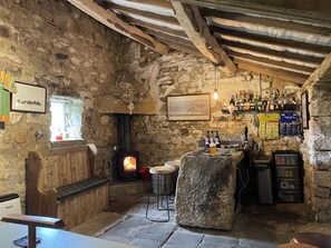 Un interior rústico con pared de piedra, banca de madera y chimenea.