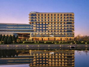 A multi-story Radisson hotel with a modern glass facade, a reflection in the water, and a landscaped front area.