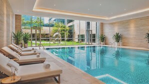 A modern indoor pool with clear glass walls, sun loungers, and potted plants. - Radisson Hotel, Beijing Daxing Airport (Daxing)