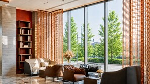 A modern lobby with a seating area, a bookshelf, and large windows offering a view of greenery and buildings. - Radisson Hotel, Beijing Daxing Airport (Daxing)