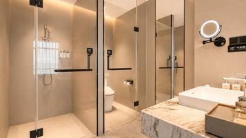 Ein modernes Badezimmer mit einer Glaskabine zur Dusche, Toilette und einem Marmor-Waschtisch mit Waschbecken und Spiegel.
