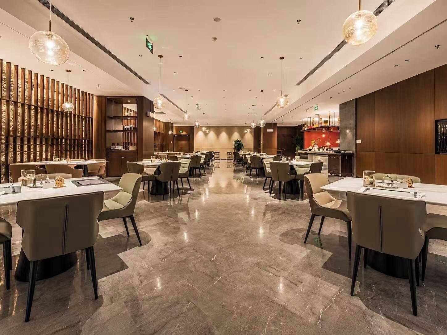 A modern restaurant with a long dining area, marble flooring, and pendant lighting.